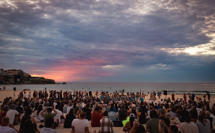 Large group of people gathered on Bondi Beach with the sun rising in the distance