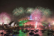Image of NYE fireworks on the Sydney Harbour Bridge with the colours of the fireworks reflected in the harbour which is dotted with boats