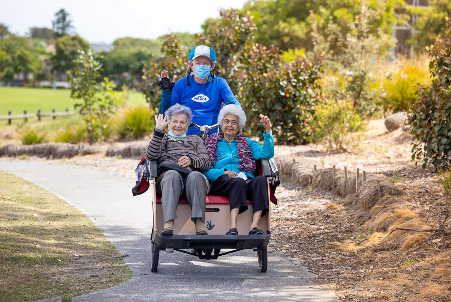 Two senior women riding inn the front of a trishaw being pedaled by someone wearing a Bike East T-shirt