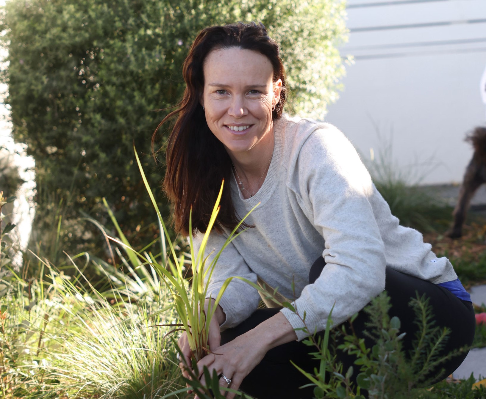 Megan crouching in her garden holding a small plant.