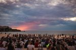 Large group of people gathered on Bondi Beach with the sun rising in the distance